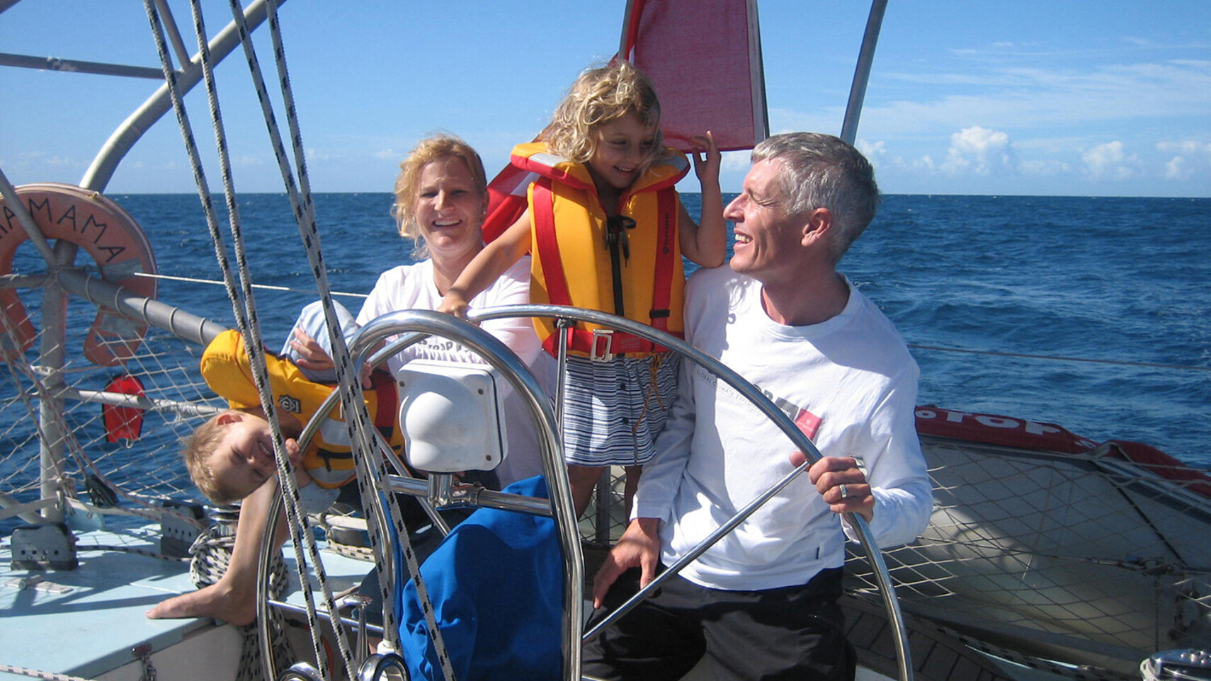 TOPtoTOP expedition family Schw&ouml;rer at the helm of their sailboat in tropical waters near Bundaberg, Australia &ndash; children wearing life jackets, sunny ocean crossing, 2009