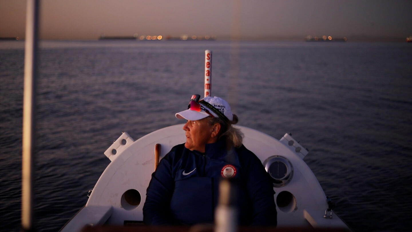 Woman in sportswear sitting on a rowing boat at dusk, gazing at the calm water.